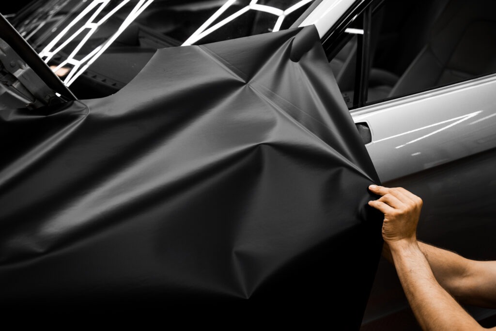 Car Door Panel Wrapping. Process of wrapping car with matte black vinyl and tensioning the material. Car wrapping starts with aligning matte black vinyl to achieve seamless coverage.